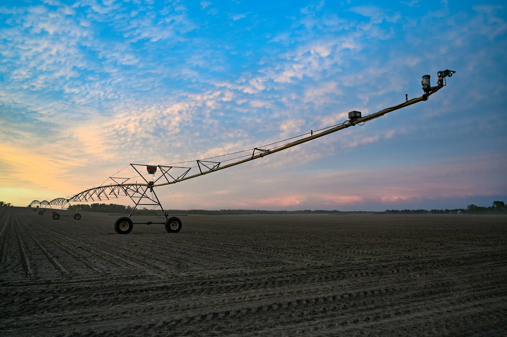 Centre-pivot irrigation line across a field at sunset