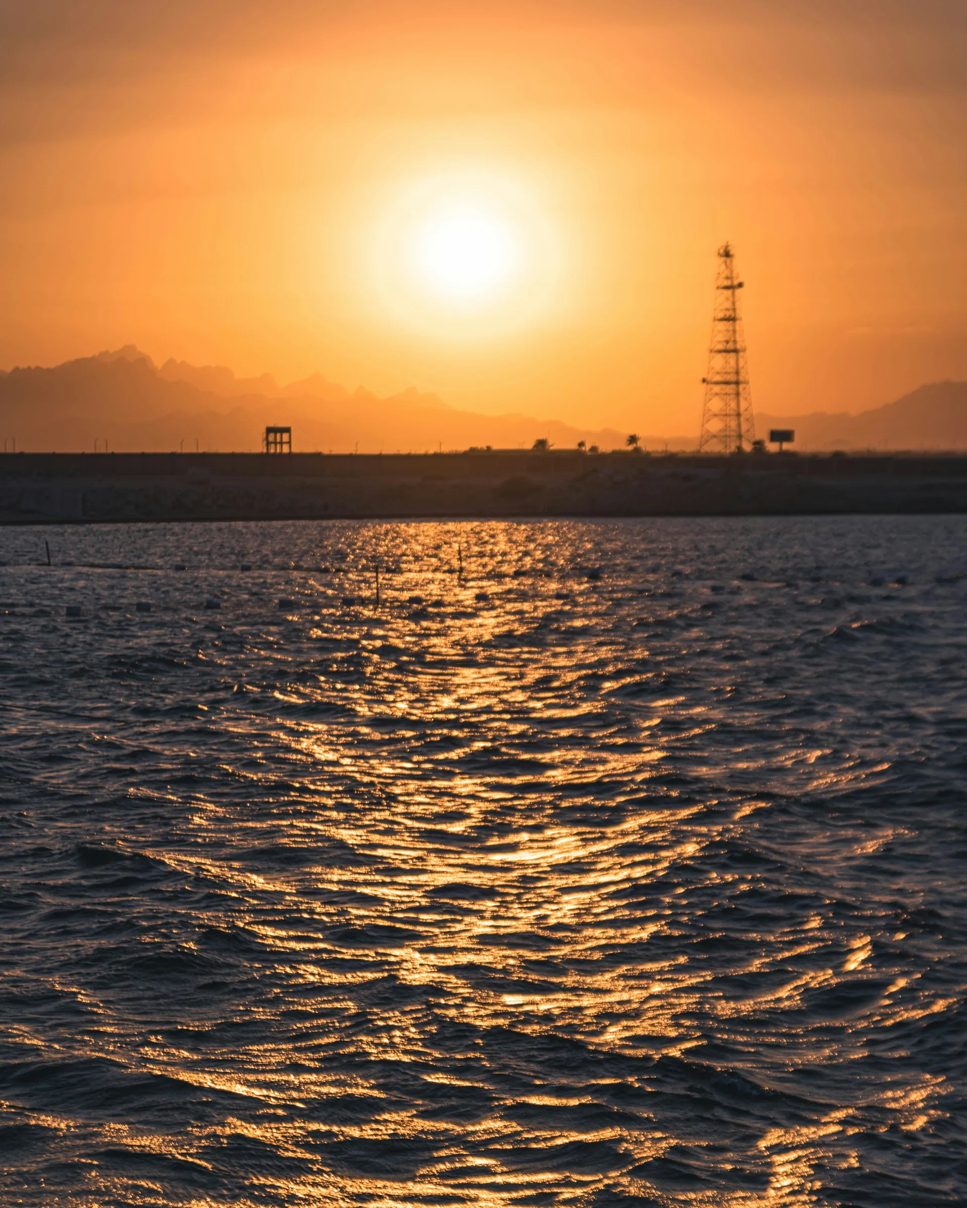 Sun setting over the sea with a coastal tower in the distance